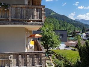 Ein mehrstöckiges Gebäude mit Balkon, Holzzaun und Blick auf ein Dorf und Berge.