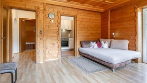 Et træpanelt interiør med en seng, en sofa, et køkken og et ur på væggen.