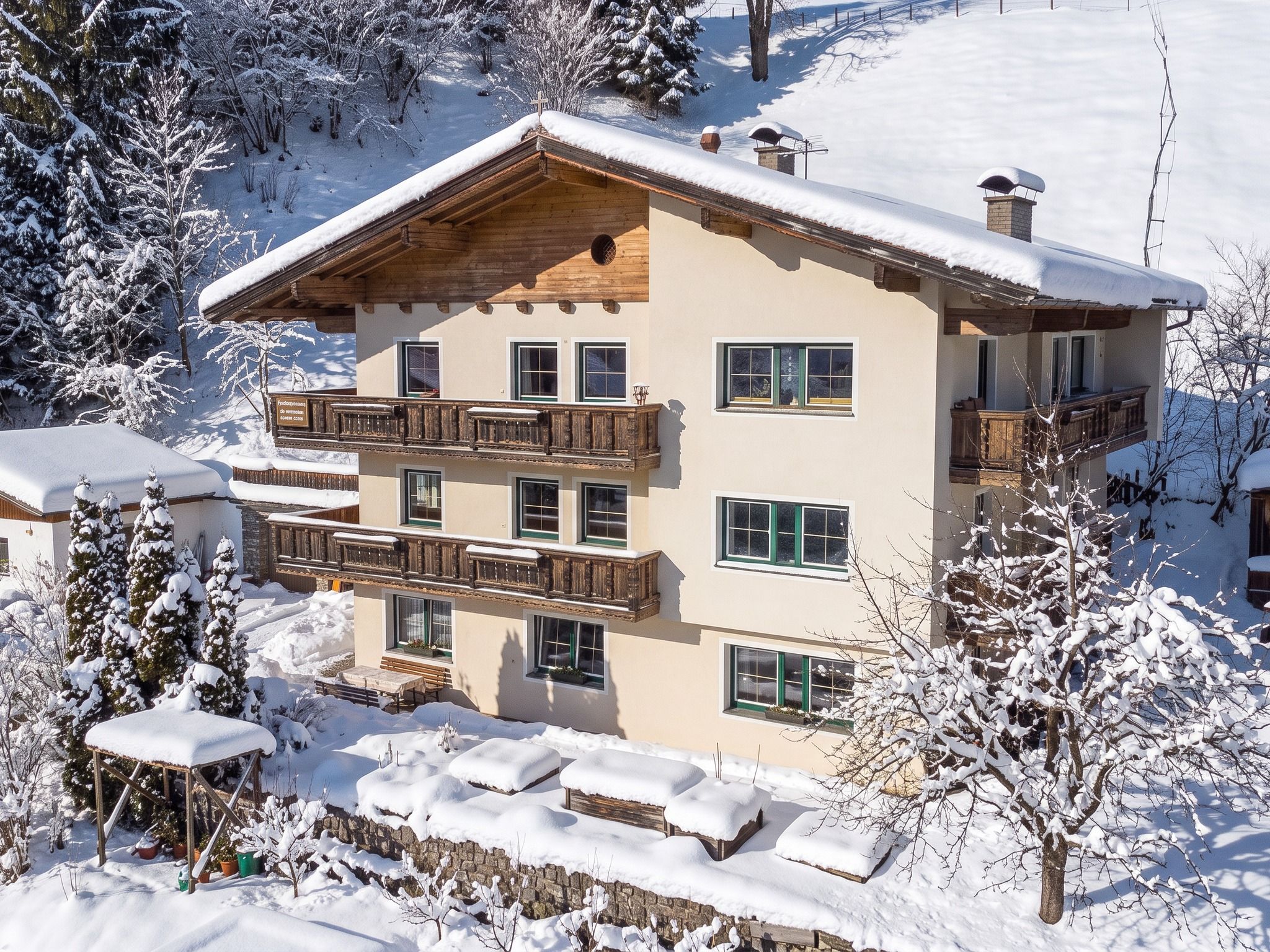 A multi-story chalet with balconies, surrounded by snow-covered trees and a ski slope in the background.
