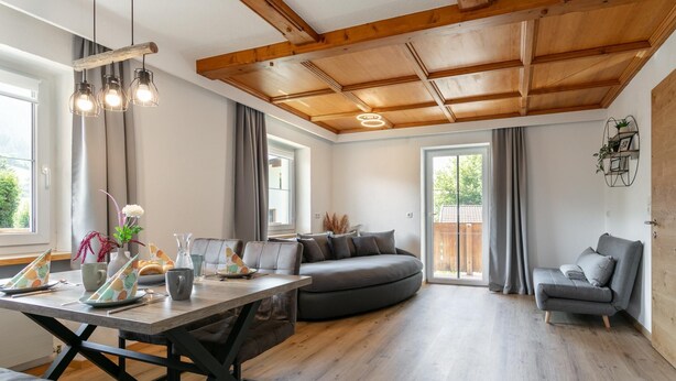 Un espacio habitable moderno con comedor, sofá, sillón y techo de madera.