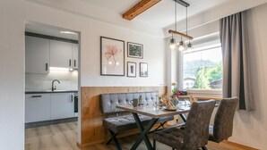 Una cocina moderna con armarios blancos, un comedor con un banco y sillas de madera, y un ventanal con vistas a zonas verdes.