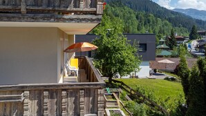 A two-story building with a balcony, a wooden fence, and a view of a village and mountains. - Dreamlike vacation apartment with sunny terrace. (Wildschönau)