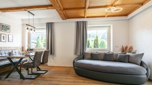 A modern living room with a wooden ceiling, a dining area with a table and chairs, and a large window with curtains. - Dreamlike vacation apartment with sunny terrace. (Wildschönau)