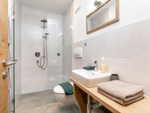 Et moderne badeværelse med brusekabine i glas, toilet, vask med håndklæde og spejl.