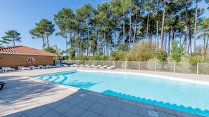A swimming pool with lounge chairs, a lifeguard tower, and tall trees in the background. - Le Domaine des Grands Lacs M48h (Parentis-en-Born)