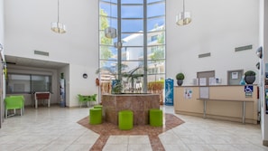 A reception area with a marble reception desk, green chairs, a large window, and indoor plants. - R Sidence Le Crystal St2s (Cagnes-sur-Mer)