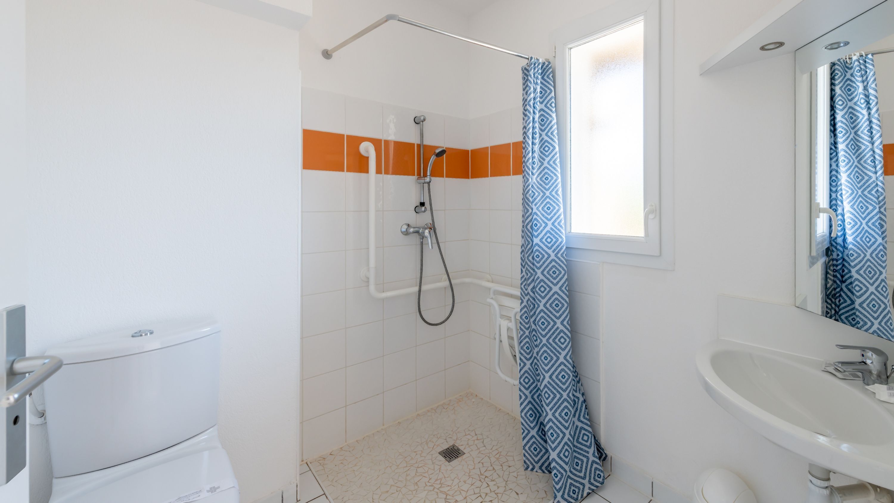 Un baño con ducha, inodoro, lavamanos y una ventana con cortina estampada.