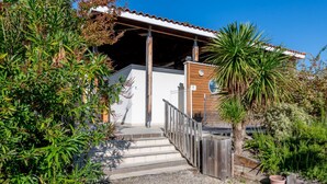 A covered outdoor area with steps leading to a wooden door, surrounded by various plants and a palm tree. - Le Domaine des Grands Lacs 2p4s (Parentis-en-Born)