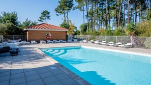 A swimming pool with lounge chairs, a lifeguard tower, and tall trees in the background. - Le Domaine des Grands Lacs M48s (Parentis-en-Born)