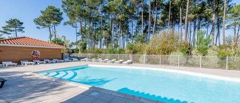En swimmingpool med solstolar, en livräddartorn och höga träd i bakgrunden.