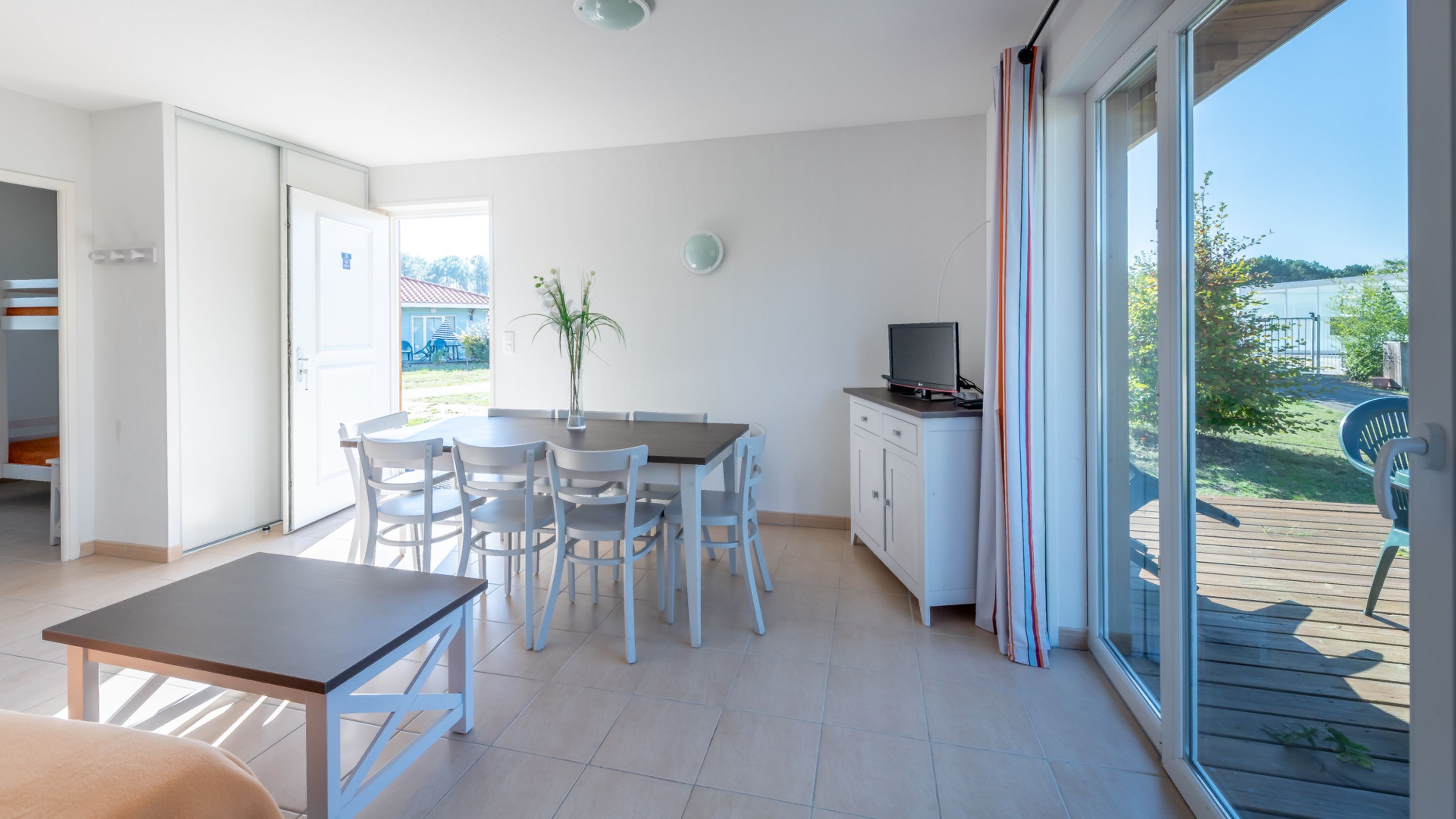 A modern room with a dining table, chairs, a TV, and a sliding glass door to a deck.