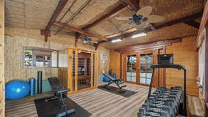 Ein Fitnessraum mit Trainingsgeräten, Holzwänden und einem Deckenventilator.