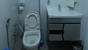 Une salle de bain comprenant des toilettes, un lavabo, un miroir, un porte-serviettes et un espace douche.