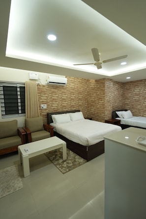 A modern hotel room with a bed, a sofa, a small table, a ceiling fan, and an air conditioning unit.