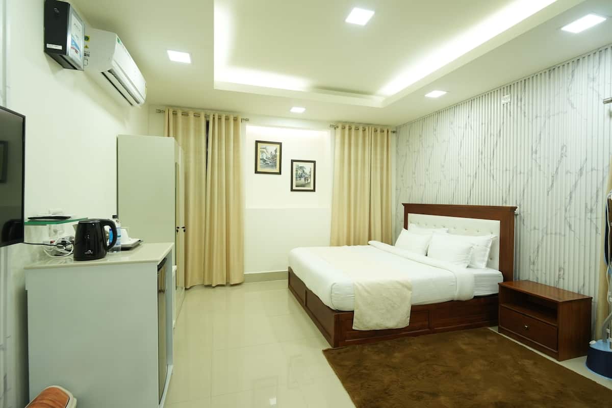 Una habitación de hotel con cama, mesita de noche, escritorio con cafetera, aire acondicionado y televisor.