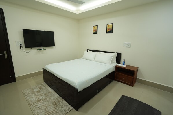 A bedroom with a bed, a TV mounted on the wall, a nightstand, and a rug. - Quality Inn (Aizawl)