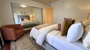 A hotel room with a bed, a chair, a mirror, and a door.