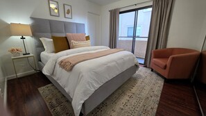 A hotel room with a bed, a nightstand, a lamp, a chair, and a view of the outside.