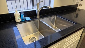 A kitchen with a stainless steel sink, a window with a view, and toiletries on the counter.