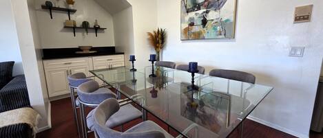 A modern dining area with a glass table, grey upholstered chairs, and a contemporary abstract painting on the wall.