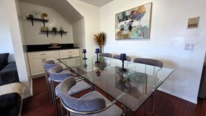 A modern dining area with a glass table, grey upholstered chairs, and a contemporary abstract painting on the wall.