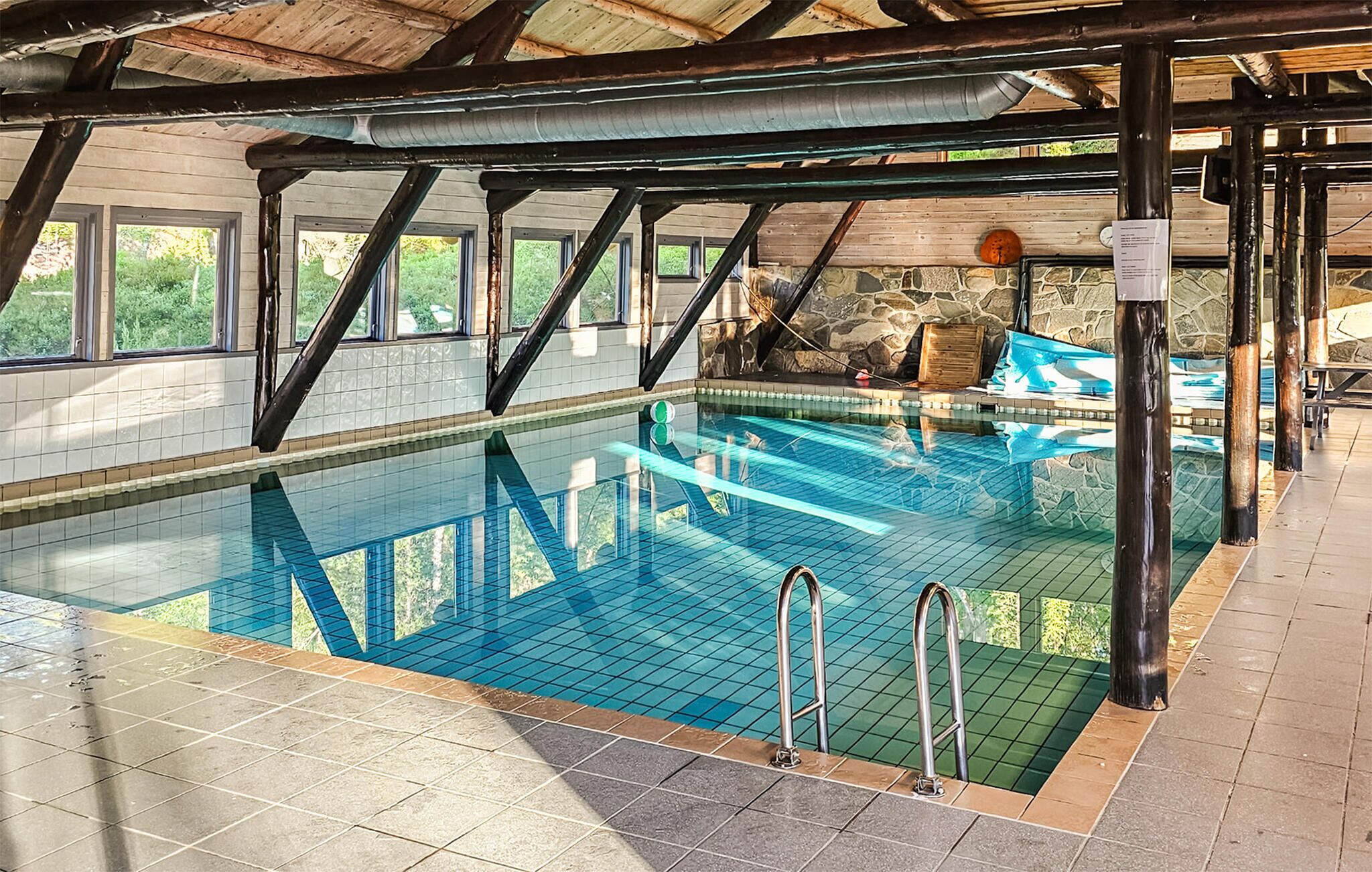 An indoor swimming pool with clear water, tiled walls, and a stone wall in the background.
