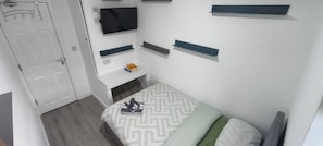 A small, neatly organized bedroom with a bed, a television mounted on the wall, and a door.