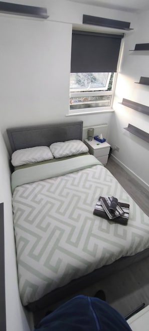 A bed with a patterned bedspread, a bedside table with a tissue box, a window with a view, and built-in shelves.