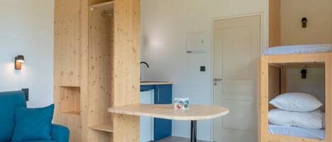 Una habitación compacta con literas, una mesita pequeña, un sofá y un armario de madera.