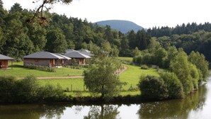 A lakeside property with multiple cabins, a grassy area, and a forested hill in the background. - Le Domaine des Mon di res 1p4v (Meyrignac-l'Eglise)