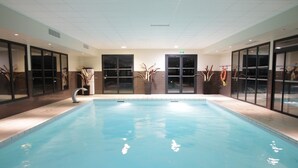 An indoor swimming pool with clear water, surrounded by glass doors and potted plants. - Le Domaine des Mon di res 1p4v (Meyrignac-l'Eglise)