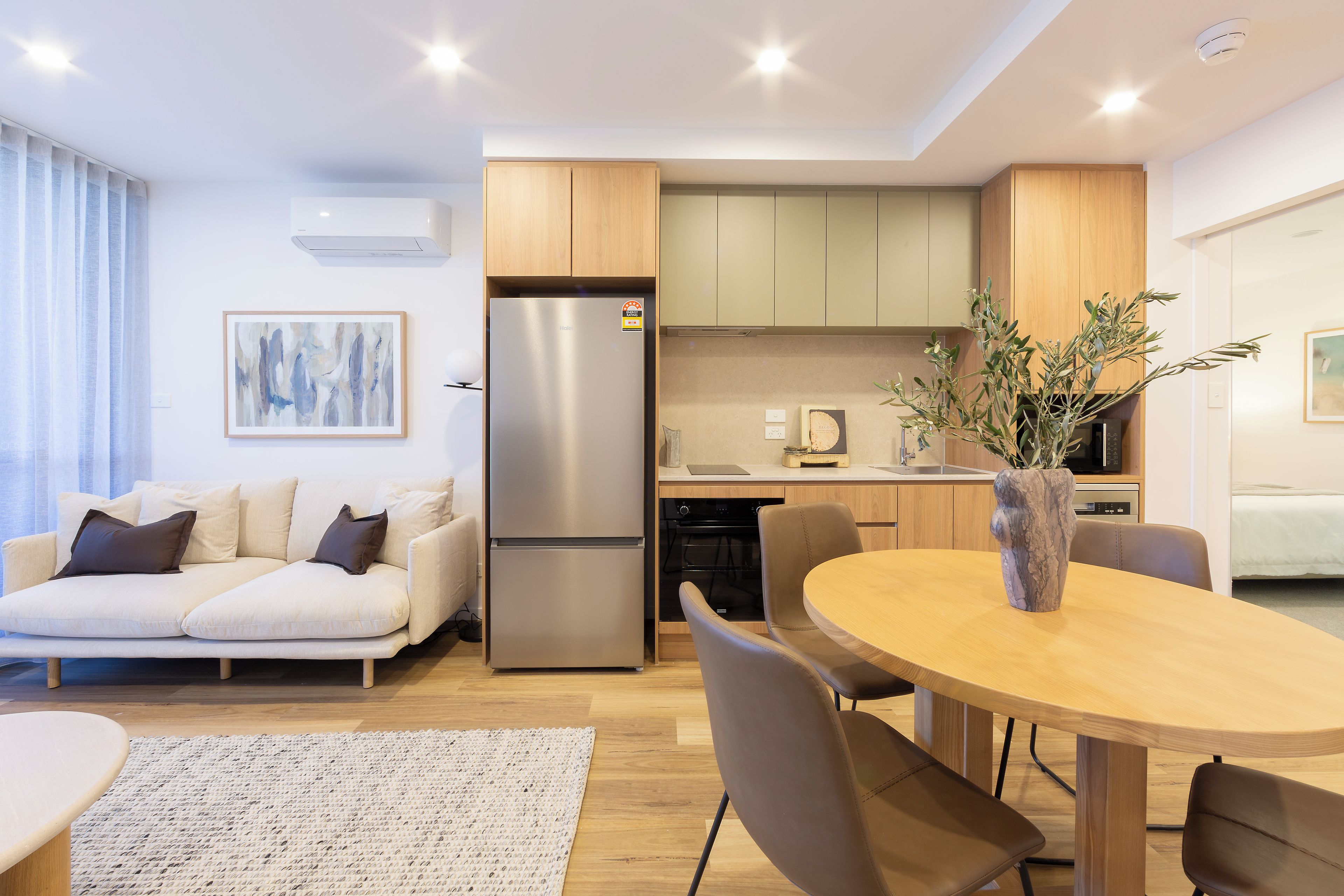 A modern kitchen with a built-in refrigerator, wooden cabinets, and a dining area with a round table and chairs.