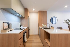 A modern kitchen with wooden cabinets, a central island, and a round mirror on the wall. - Canopy Collective Serviced Apartments (Phillip)