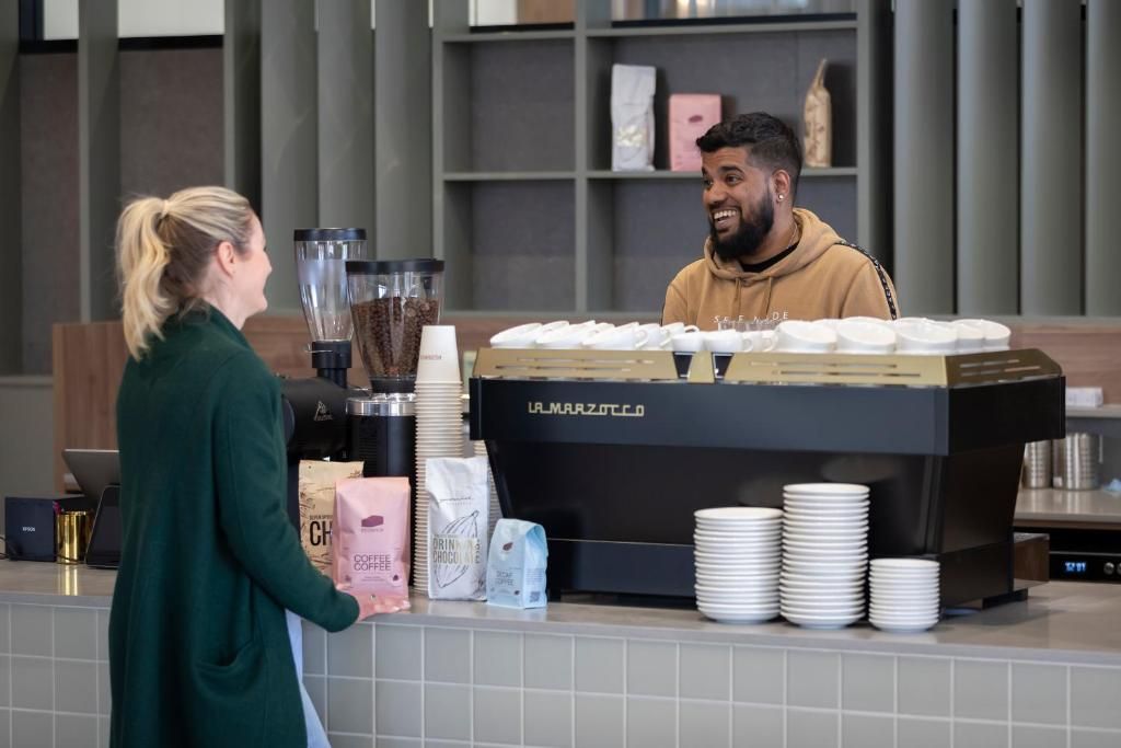 Ein Tresen in einem Café mit einer Kaffeemaschine, Stapeln weißer Tassen sowie Säcken mit Kaffee und Schokolade.