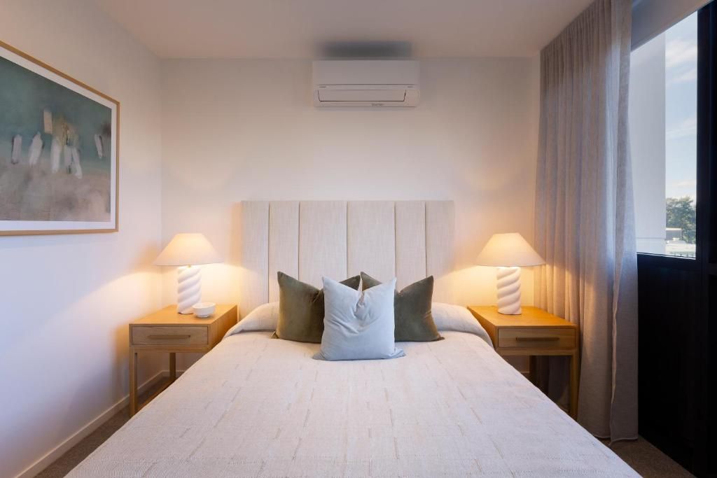 Een hotelkamer met een groot bed, twee nachtkastjes, een hoofdbord, een airconditioning en een schilderij aan de muur.