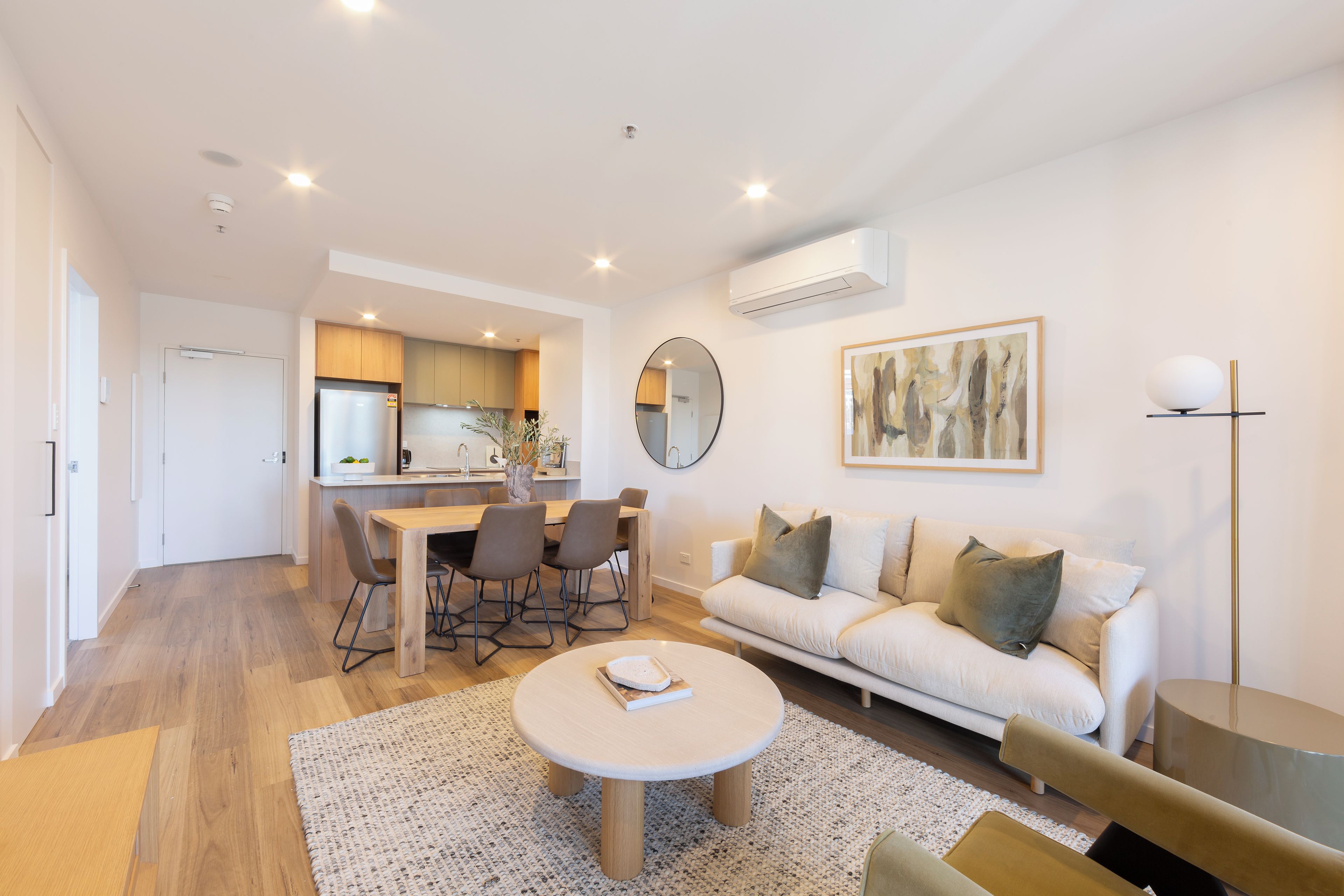 Un salon moderne avec un canapé, une table basse et un coin repas comprenant des chaises, et une cuisine en arrière-plan.