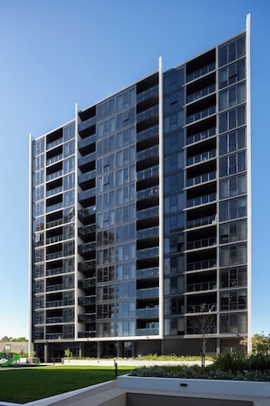 A modern high-rise building with multiple balconies, a flat roof, and a landscaped area with grass and plants. - Canopy Collective Serviced Apartments (Phillip)