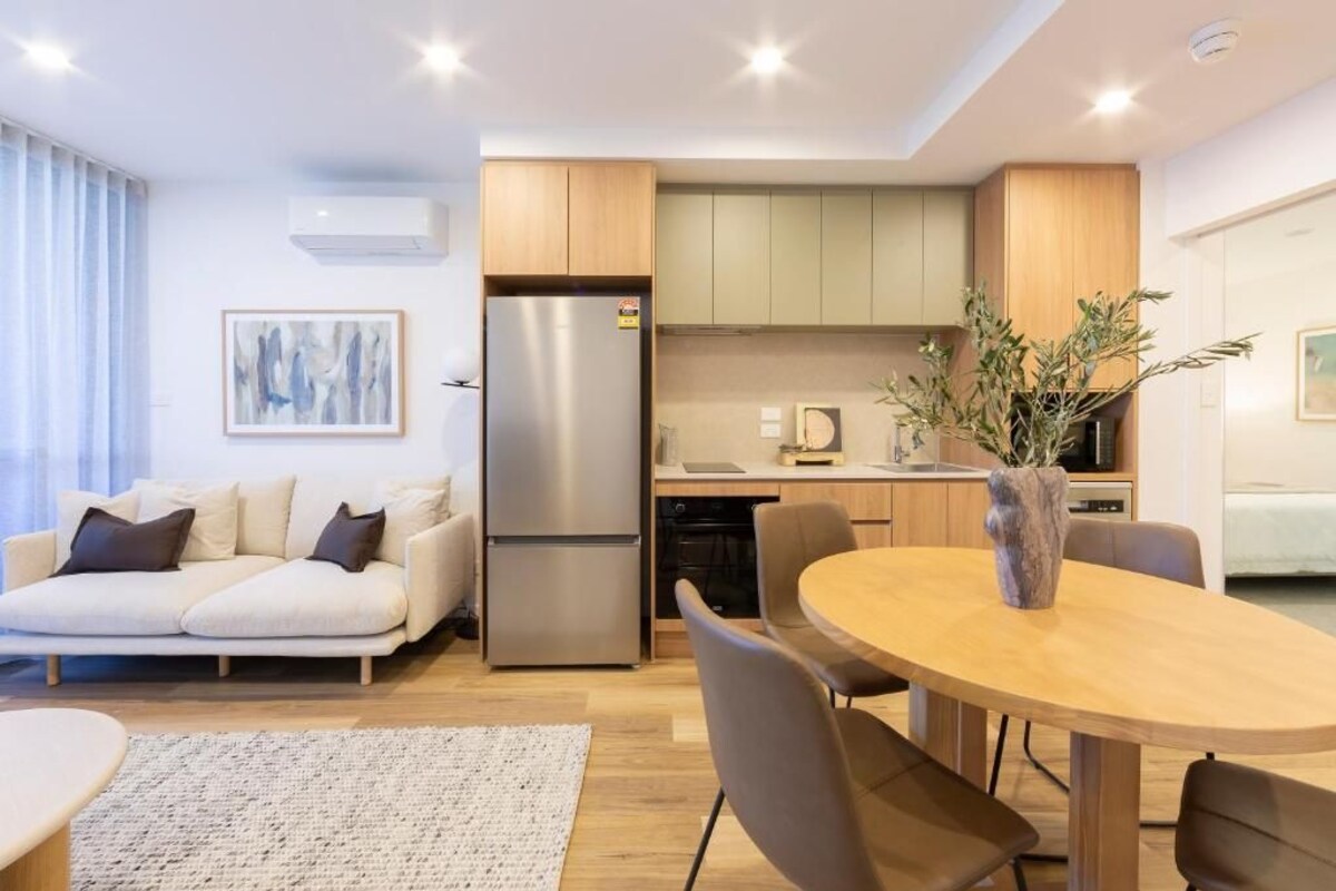 Uma sala de estar moderna com sofá, mesa de jantar e cadeiras. Há também uma cozinha com armários e eletrodomésticos.