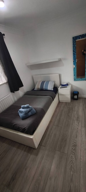 Quarto com cama, mesa de cabeceira e um cesto de lixo pequeno.