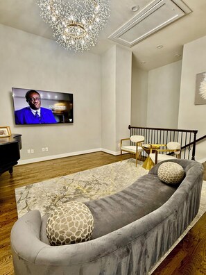 Ein modernes Wohnzimmer mit grauem Sofa, einer Kristallleuchter, einem Fernseher und einem Klavier.