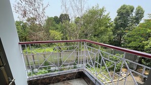 A balcony with a white metal railing, a marble floor, and a view of greenery and trees. - Jonaki Shantiniketan (Bolpur)