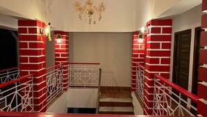 A staircase with red brick walls and white railings, a chandelier, and wall-mounted lights. - Jonaki Shantiniketan (Bolpur)