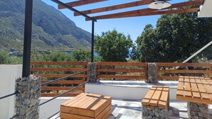An outdoor patio with wooden furniture, a pergola, and a view of mountains and greenery. - Cozy 1-bedroom apartment in charming Kalymnos with AC (Kalymnos)