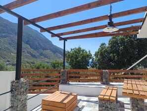 An outdoor patio with wooden furniture, a pergola, and a view of mountains and greenery. - Cozy 1-bedroom apartment in charming Kalymnos with AC (Kalymnos)