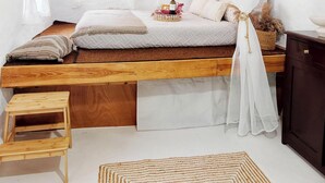 A bedroom with a wooden bed, a small wooden stool, a woven rug, and a TV mounted on the wall. - Cozy 1-bedroom apartment in charming Kalymnos with AC (Kalymnos)