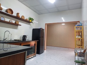 Une cuisine avec un réfrigérateur noir, un évier avec un robinet, un plan de travail en bois et une étagère ornée d’objets décoratifs.