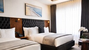 A hotel room with two beds, a large headboard, a painting, a telephone, and a plant.
