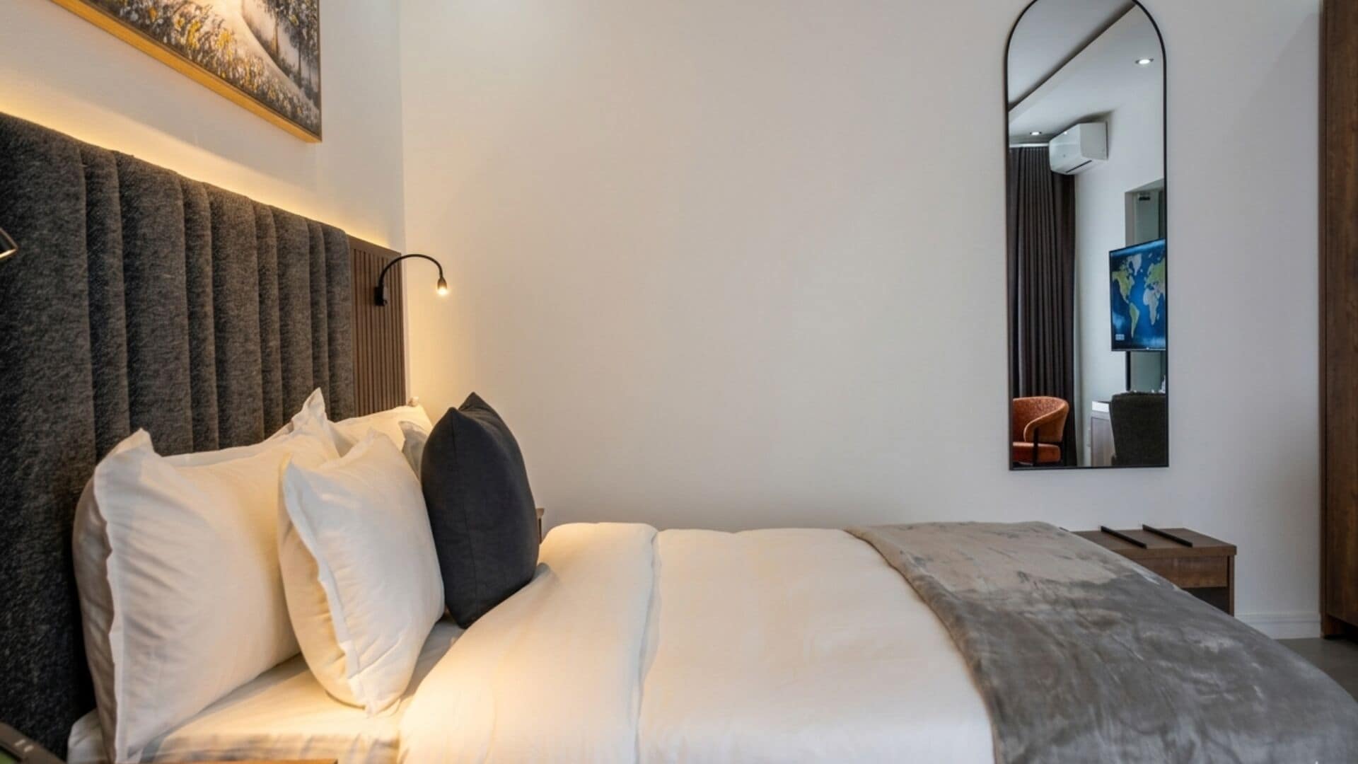 Una habitación de hotel moderna con una cama grande, cabecera, mesita de noche, espejo y un mapa mundial en la pared.