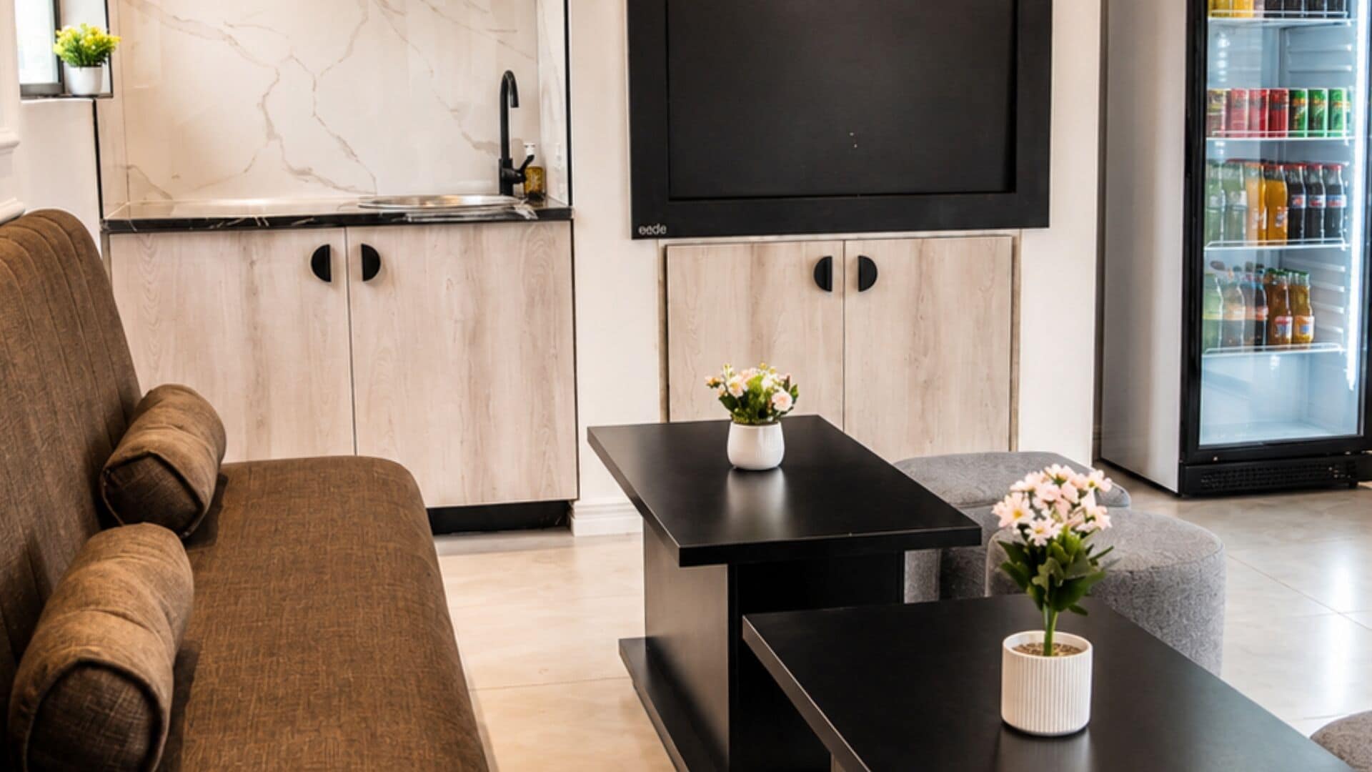 A modern living room with a sofa, a coffee table with a vase, a flat-screen TV, and a mini-fridge.