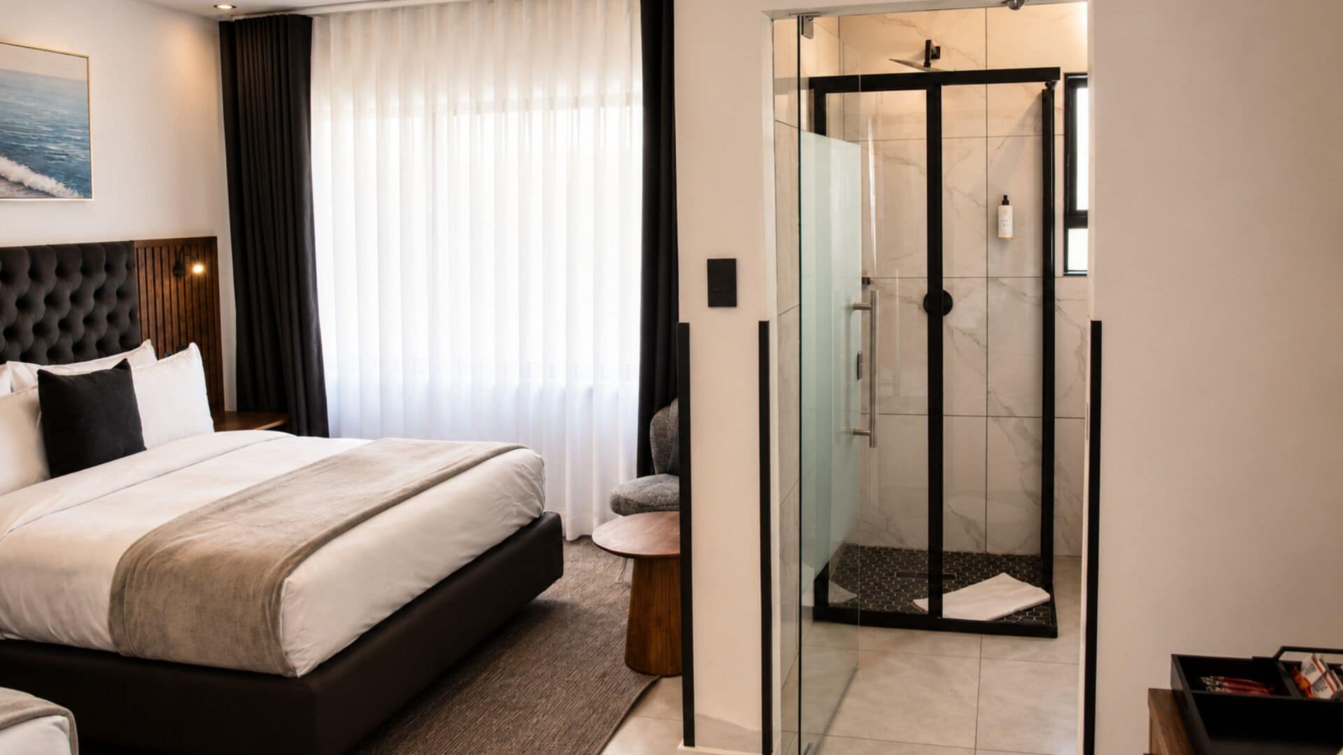 A hotel room with a bed, a shower, and a glass-enclosed shower area.